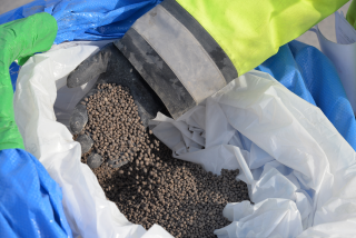 Industrial employee holding TIMAC AGRO high-efficiency granular fertilizers from an open bag.