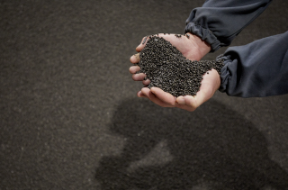 Industrial employee holding TIMAC AGRO high-efficiency granular fertilizers from a fertilizer pile.